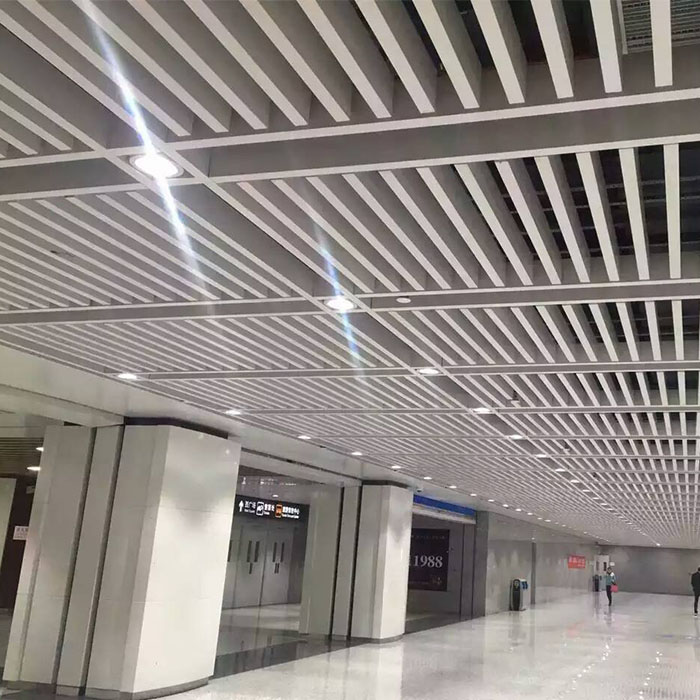 White linear aluminum baffle ceiling with integrated lighting above a transit concourse