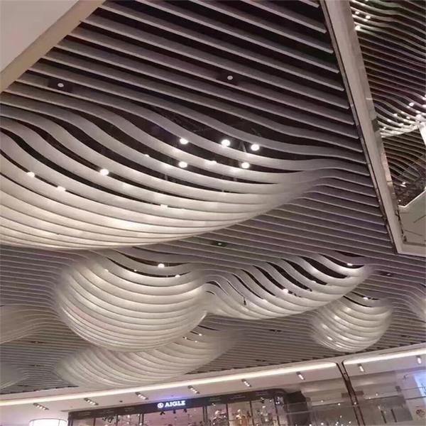 Silver curved aluminum baffles forming waves across a shopping interior ceiling