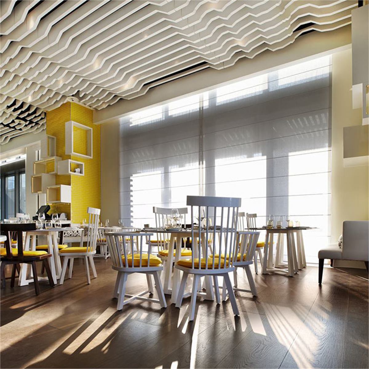 White stepped ceiling baffles arranged above a sunlit restaurant dining space