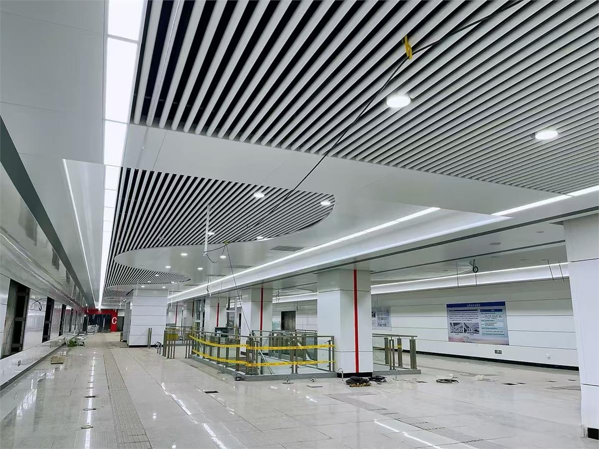 White aluminum baffle ceiling with integrated lighting above a transit concourse during installation